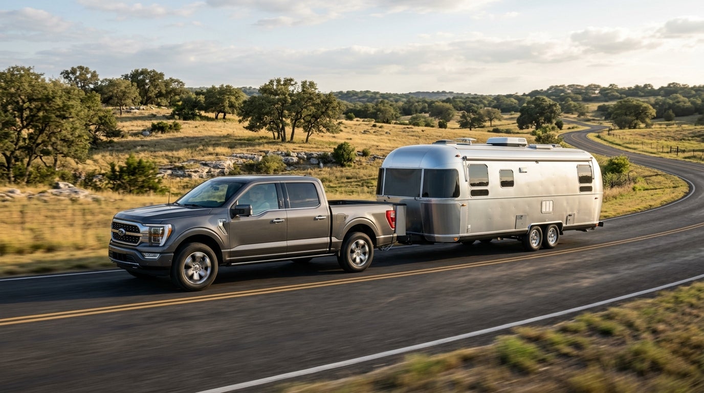 Dark grey Ford F-150 pickup truck towing a silver Airstream trailer along a rural two-lane road. (Representative image for illustration purposes only. Actual vehicle may vary based on trim and configuration.)