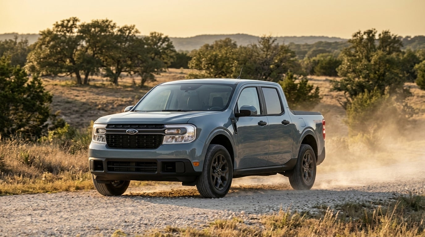 A blue-grey Ford Maverick pickup truck driving along a dusty gravel road in a rural landscape. (Representative image for illustration purposes only. Actual vehicle may vary based on trim and configuration.)