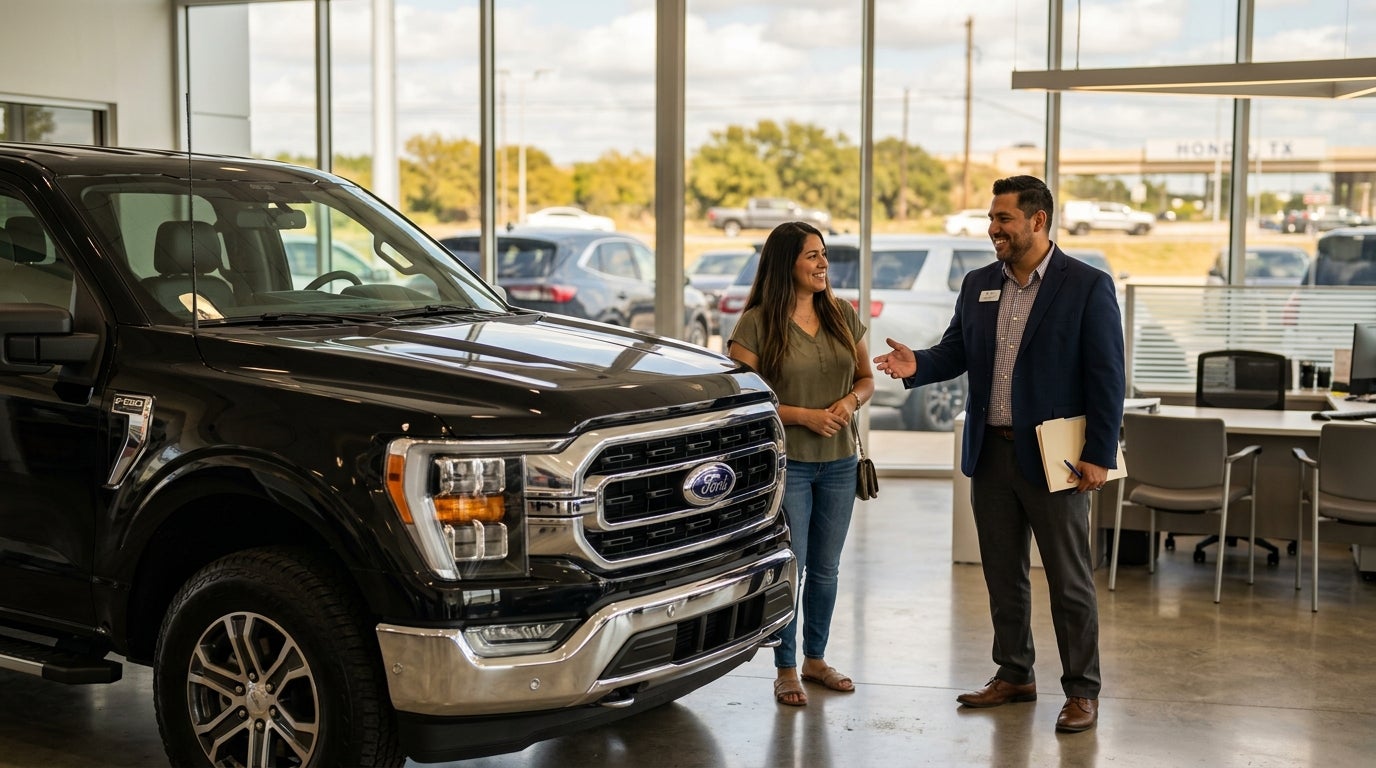A car salesman gesturing towards a black Ford truck while talking to a female customer inside a dealership showroom. (Representative image for illustration purposes only. Actual vehicle may vary based on trim and configuration.)